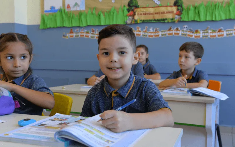 İlkokul öğrencisi sınıfta defterine yazı yazarken gülümsüyor